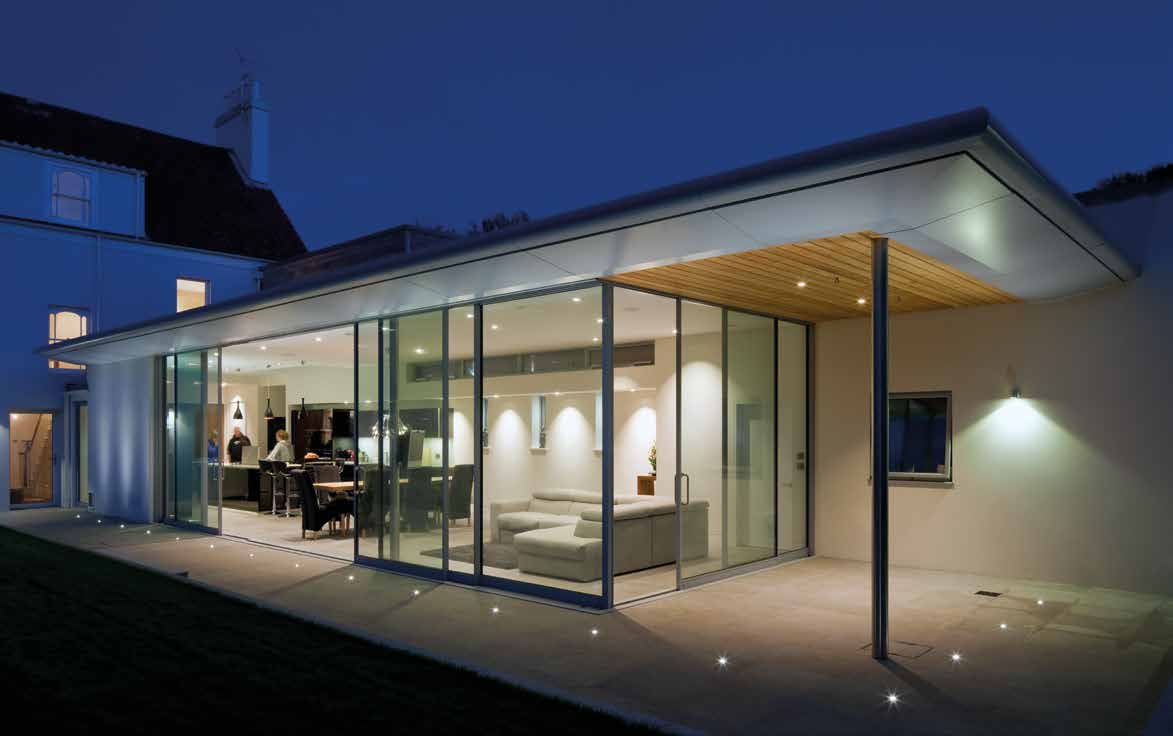 Illuminated contemporary home with sliding glass doors meeting at a glazed corner and opening onto a terrace